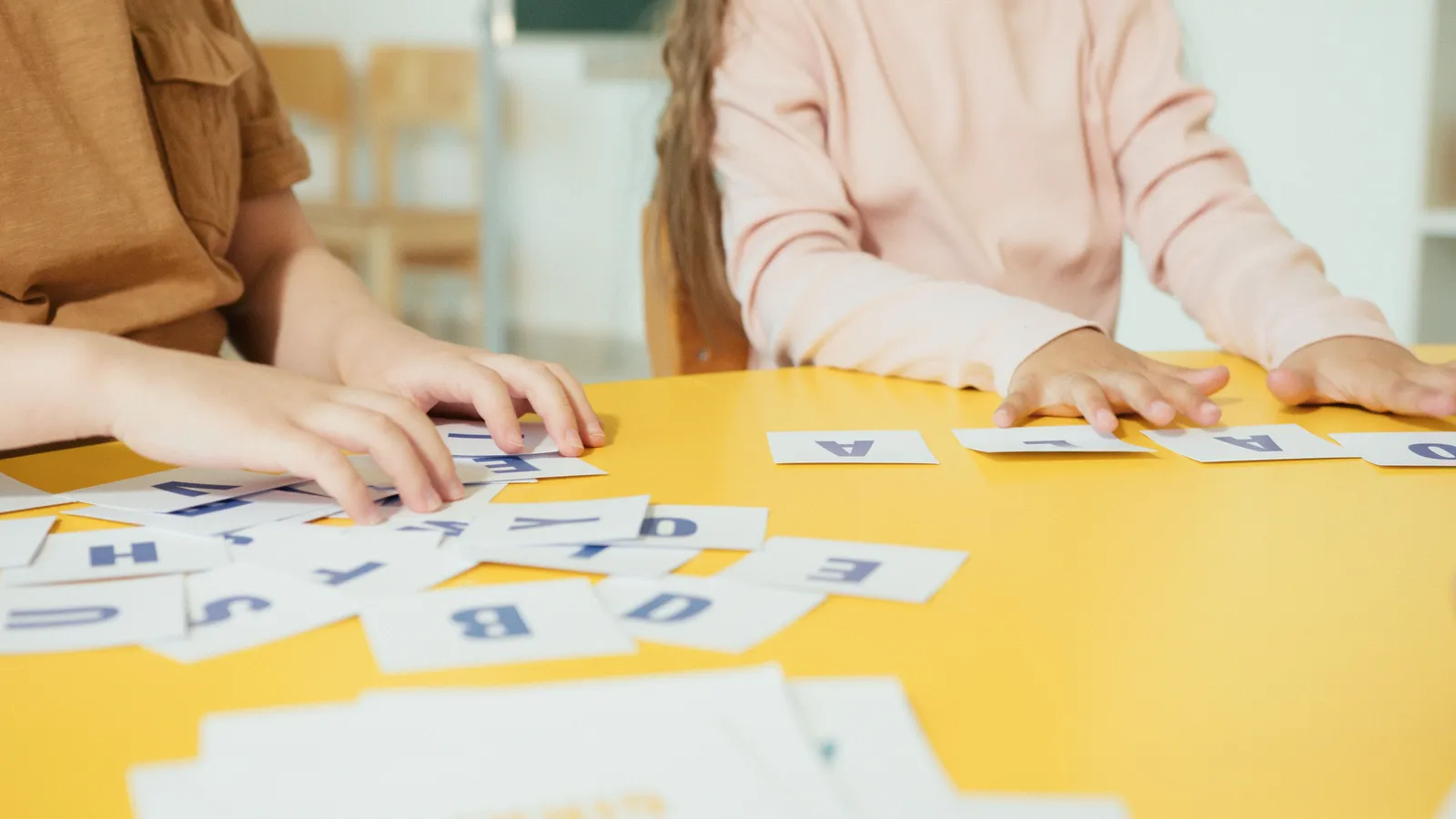 Dos niños forman palabras con tarjetas de letras sobre una mesa amarilla